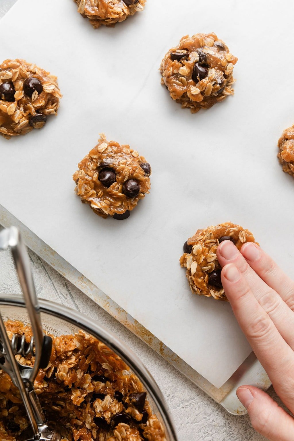 Overhead view of a sheet pan lined with parchment paper and a hand forming cookies on the pan.