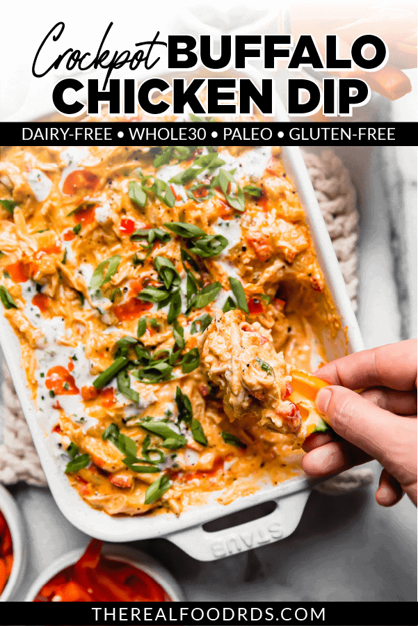 Buffalo chicken dip served in a white baking dish topped with ranch, hot sauce, and green onions and being scooped up with a vegetable.