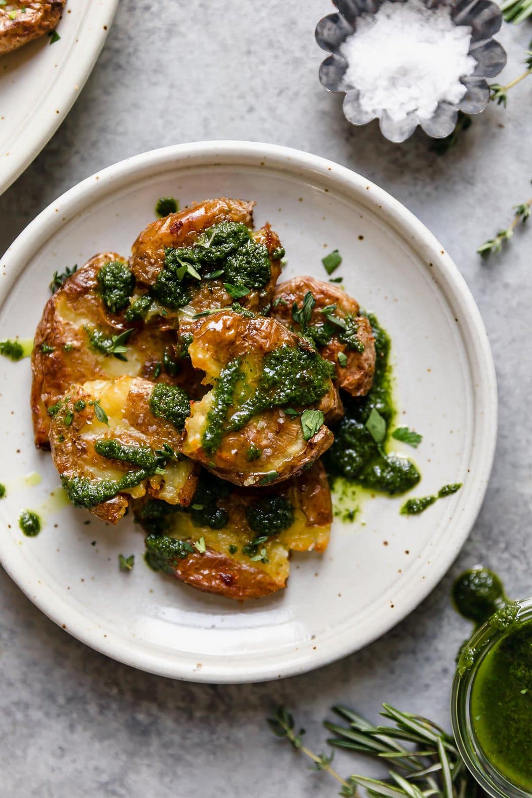 Crispy smashed potatoes topped with garlic-herb oil on a speckled cream plate.