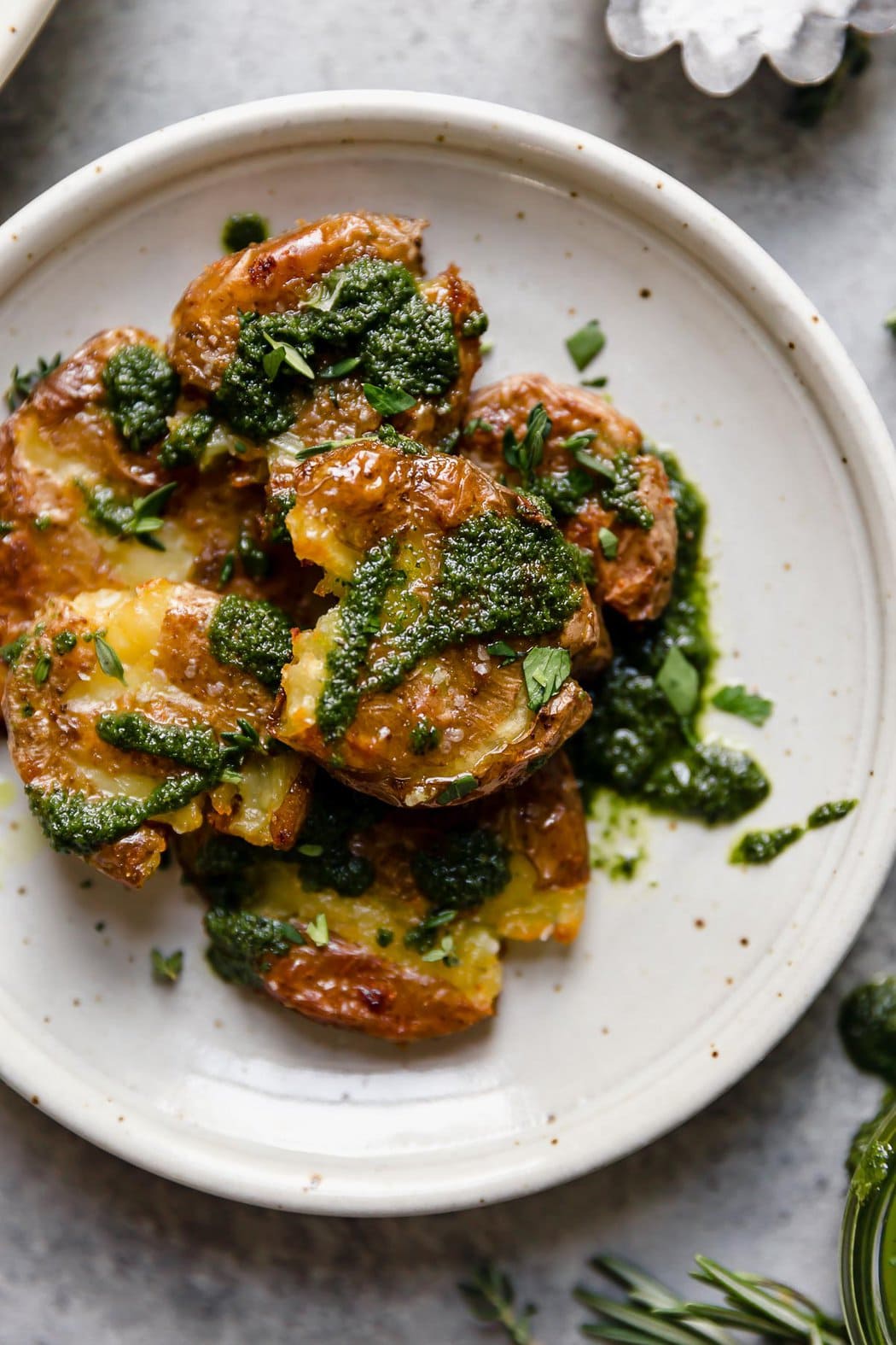 A speckled cream plate filled with crispy smashed potatoes with a side of garlic-herb sauce.
