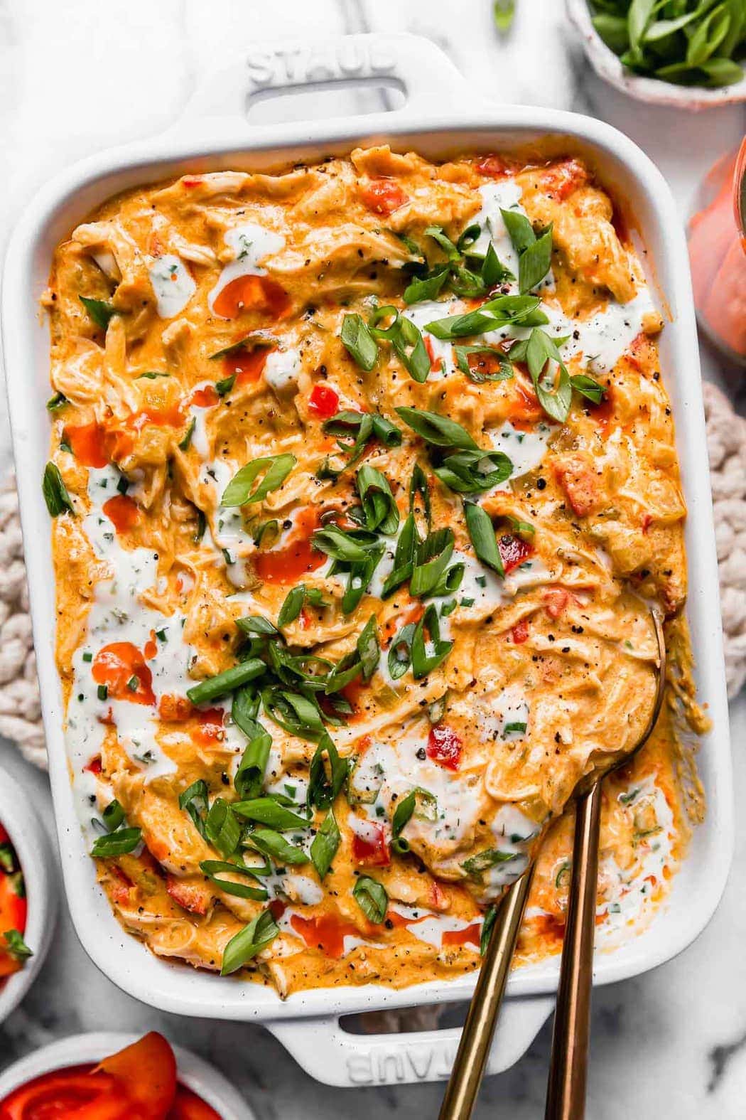Creamy buffalo chicken dip topped with buffalo sauce, green onions, and ranch dressing