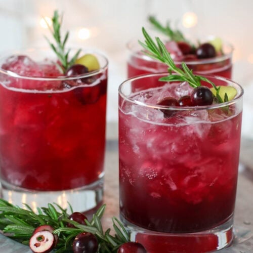 Three clear drink glasses filled with sparkling cranberry kombucha mocktail and garnished with fresh cranberries and rosemary sprigs.