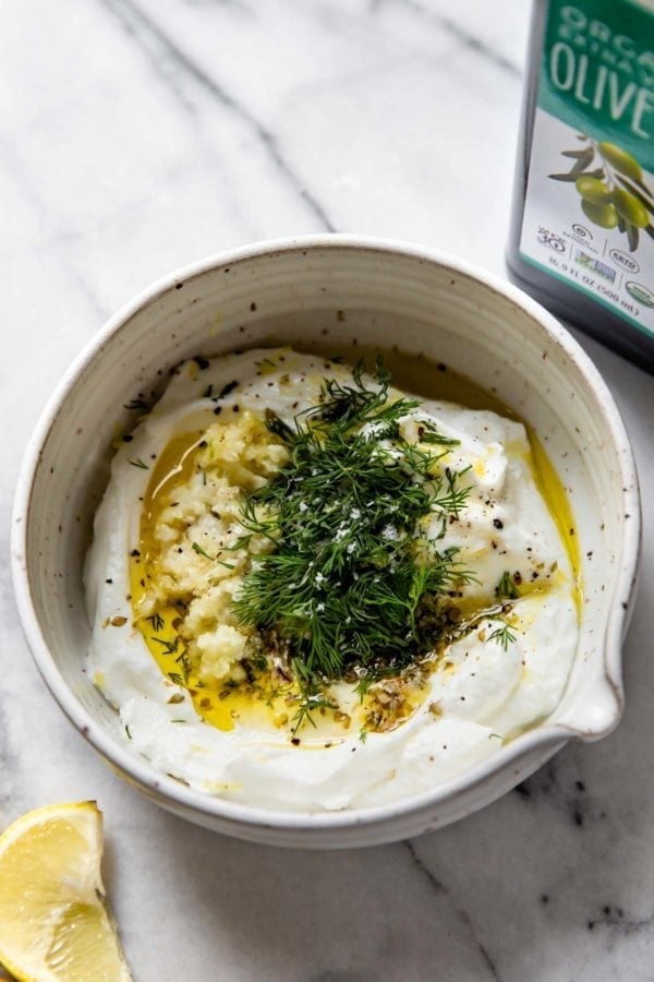 Overhead view of tzatziki sauce next to a bottle of olive oil