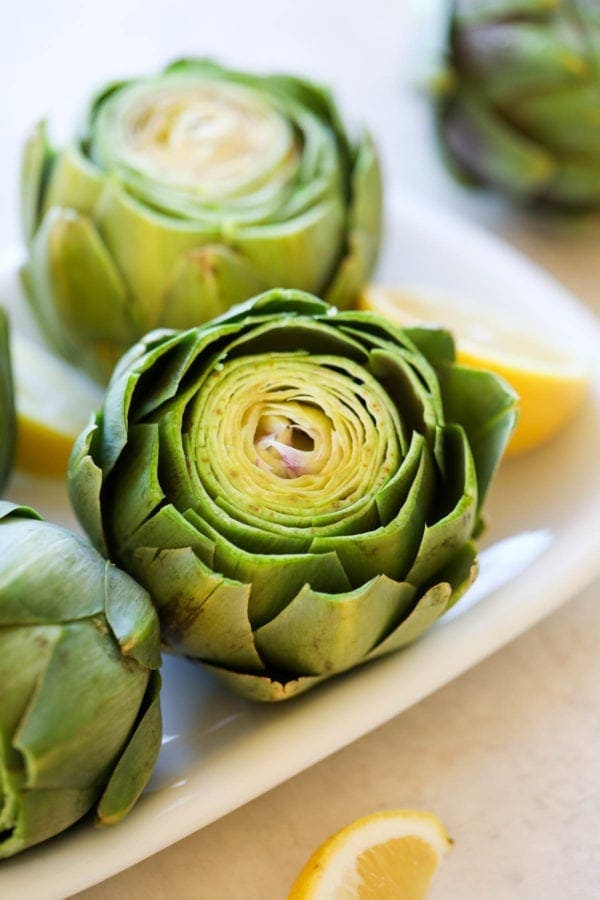 A white tray filled with green artichokes washed and cut and ready for the Instant Pot.