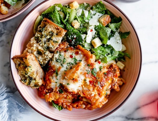 Overhead view of easy skillet lasagna in a bowl with a side salad and garlic bread