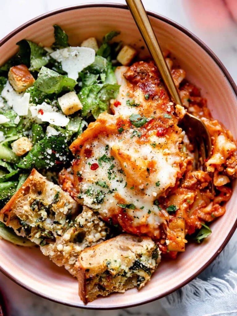 Overhead view of a plate filled with a Ceasar salad next to lasagna layers and garnished with garlic cheese bread. 