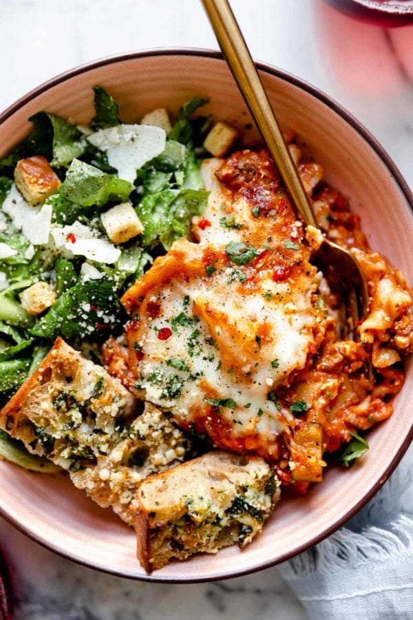 Easy Skillet Lasagna served in a ceramic bowl on top of Romaine lettuce with garlic bread and shaved parmesan on the side