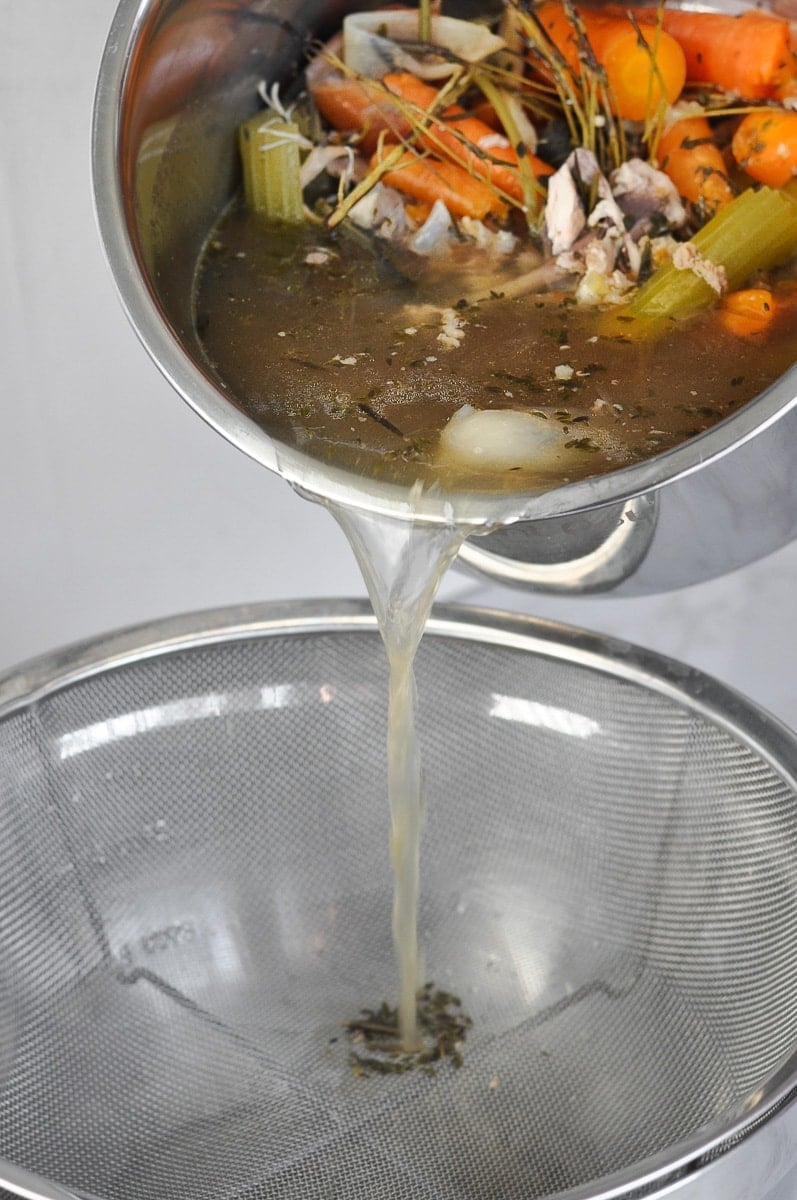 Bone broth being strained through a mesh colander 