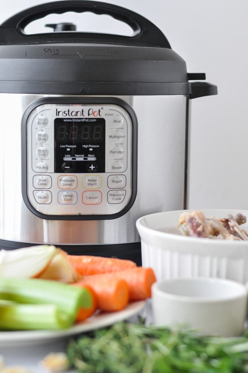 An Instant Pot in the background with all ingredients for homemade bone broth in the forefront 