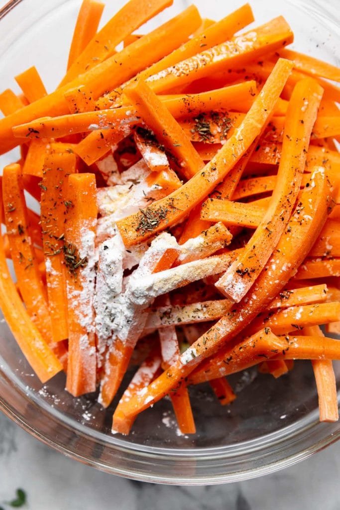 Ingredients for baked carrot fries in a mixing bowl