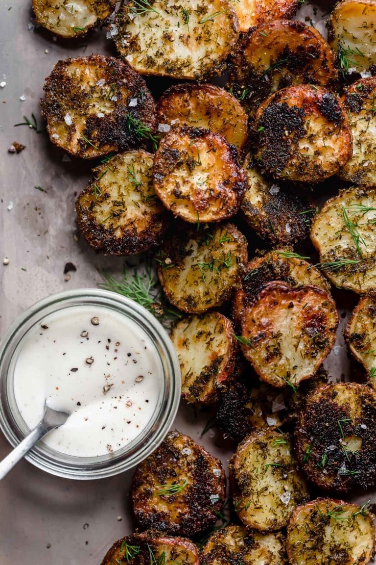 Overhead view of a sheet pan with crispy roasted potatoes and a small ramekin of ranch dipping sauce. 
