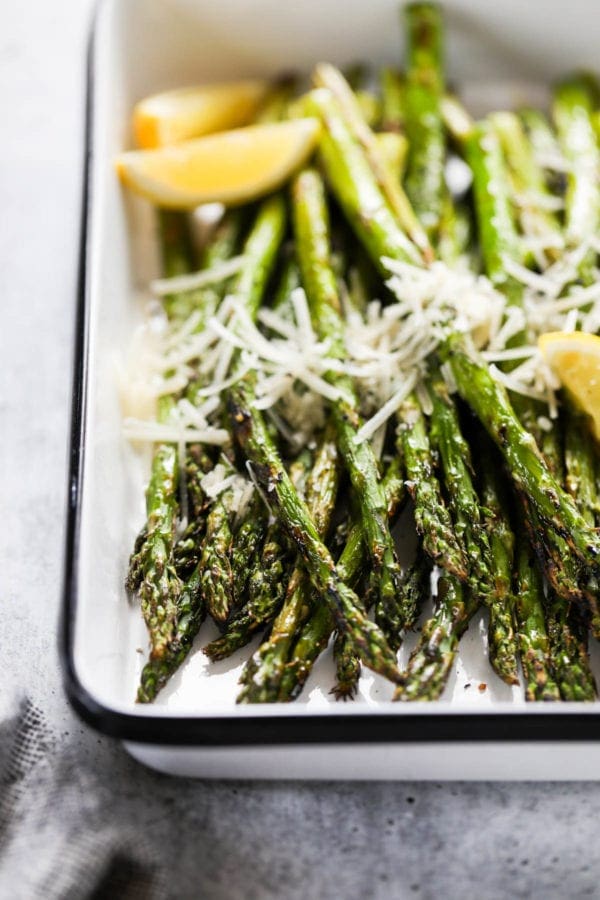 Close up view of grilled asparagus topped with fresh grated parmesan cheese and lemon wedges
