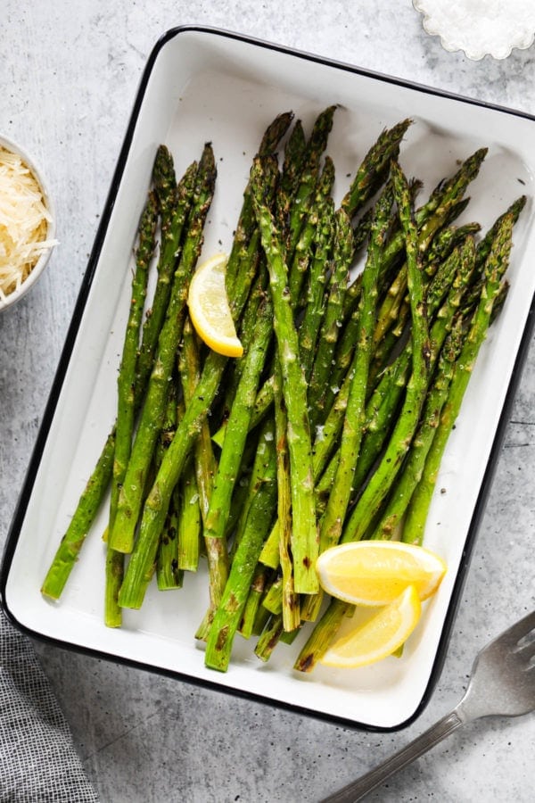 Grilled asparagus spears and lemon wedges topped with salt and pepper in a grill pan