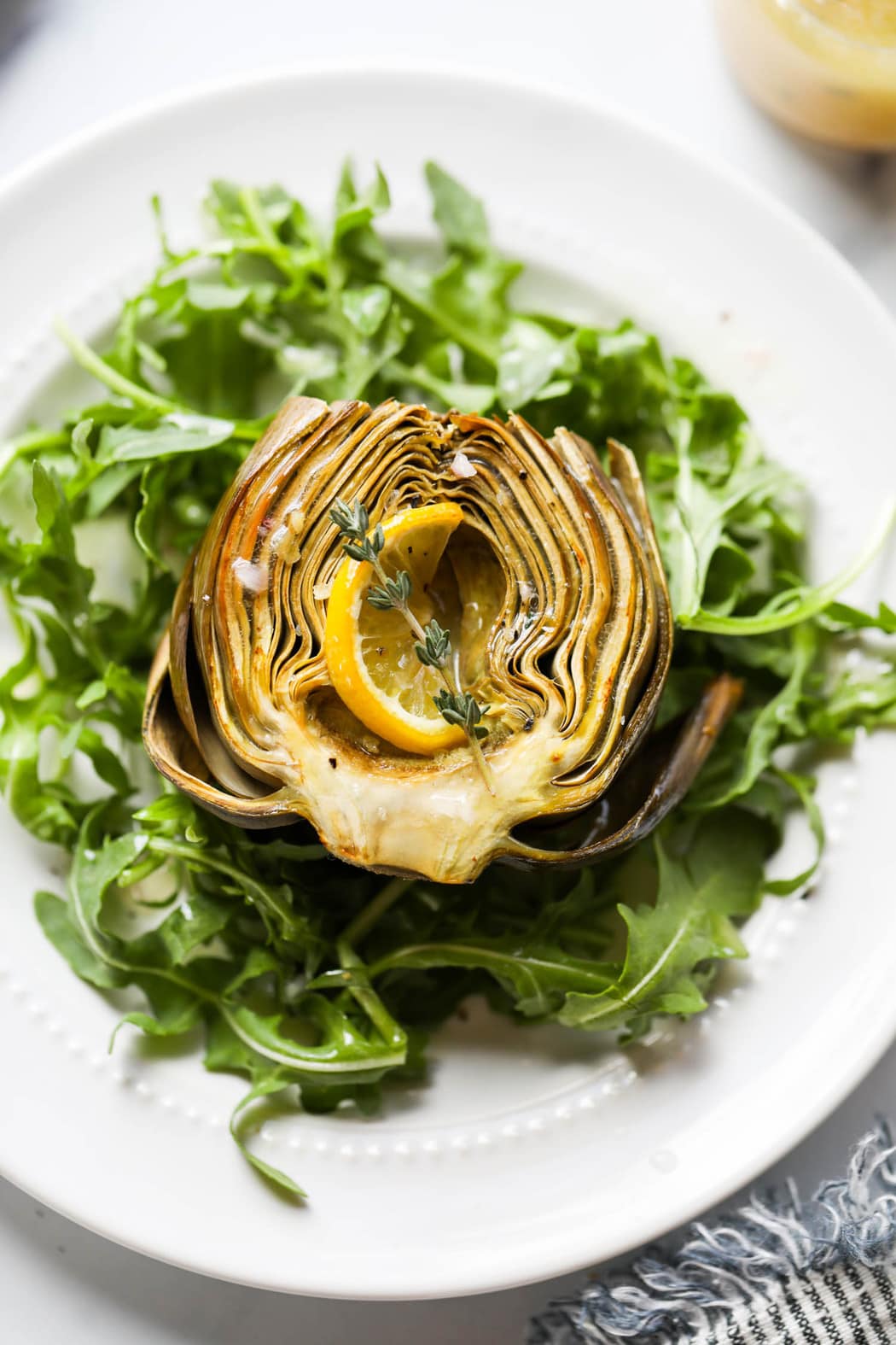 Overhead view of a roasted artichoke on top of arugula.