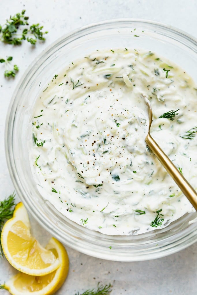 Creamy homemade Tzatziki sauce in a glass bowl topped with black pepper and fresh dill weed.