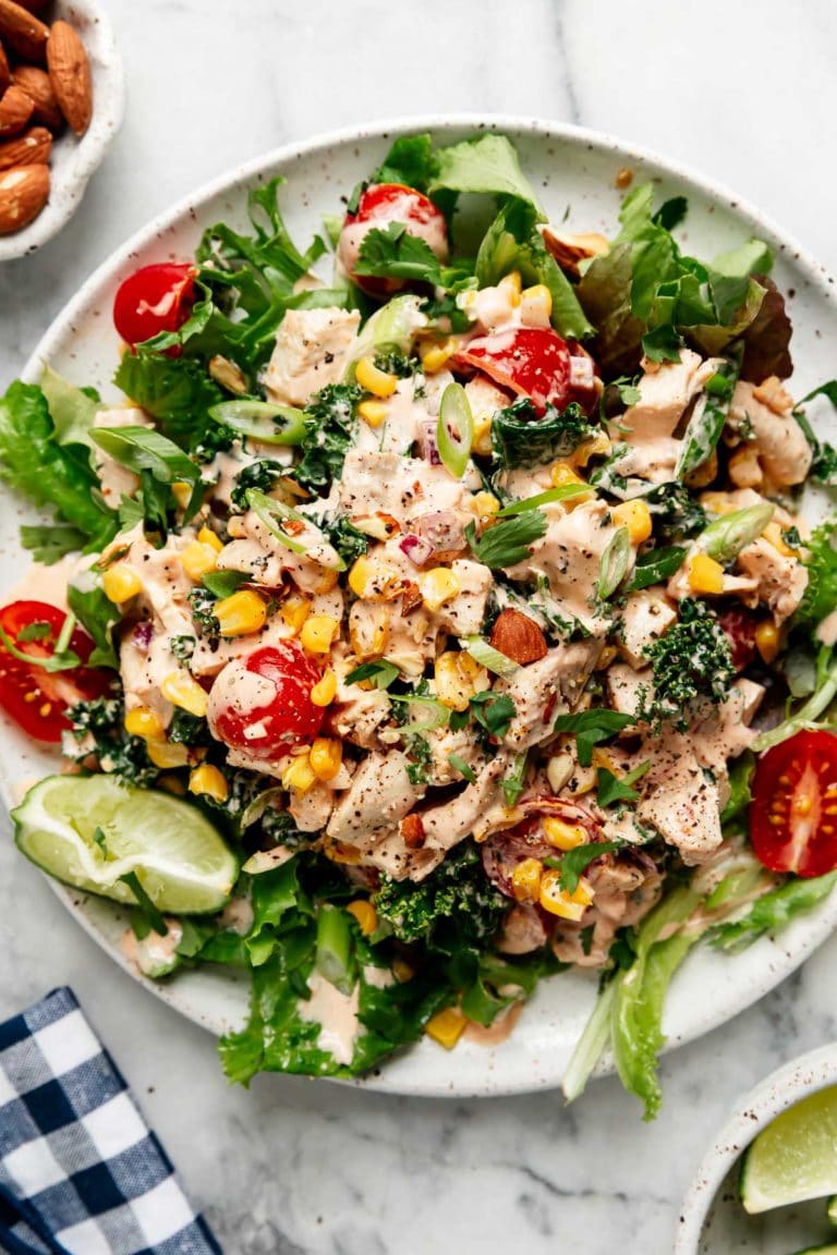 Overhead view of a plate filled with greens topped with tender chicken, juicy grape tomatoes, sweet corn kernels and topped with a creamy BBQ dressing.