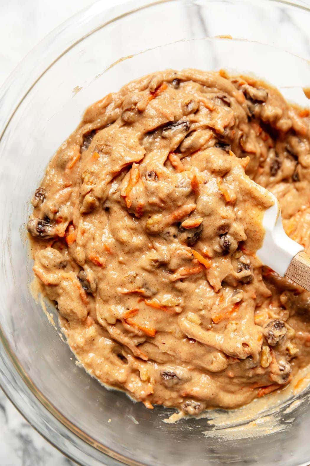 The batter for carrot cake bars in a mixing bowl with a spatula in the batter