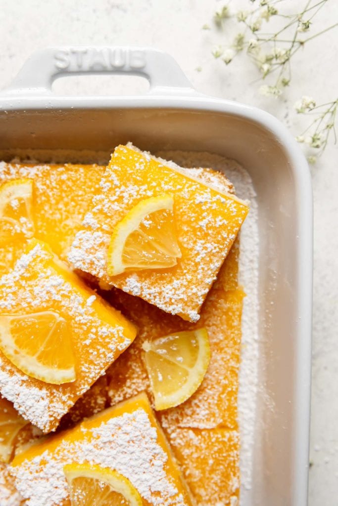 Lemon bars with a gluten-free shortbread crust cut into bars in a white baking dish