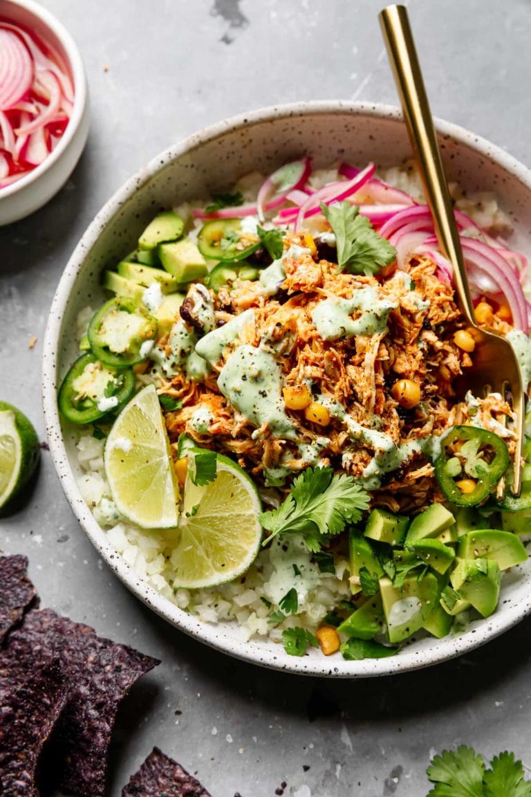 Instant pot salsa chicken served on top of cauliflower rice, mixed greens, jalapeno, and topped with cilantro lime crema