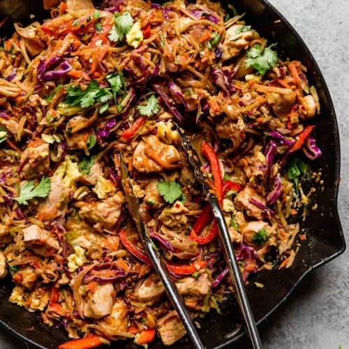 Overhead view chicken pad thai in skillet with tongs in skillet