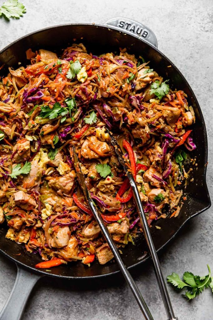 Overhead view chicken pad thai in skillet with tongs in skillet