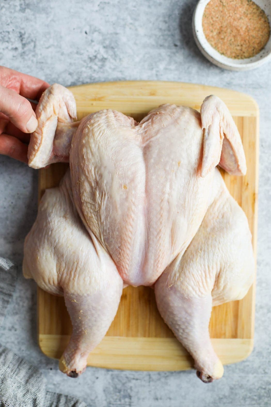 A raw whole chicken with wings being secured up and over for grilling