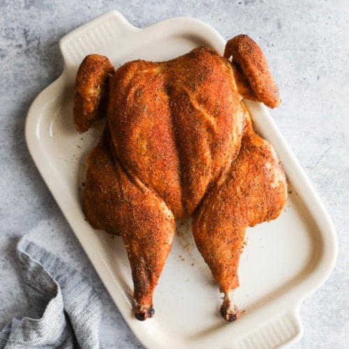 Freshly grilled and smoked spatchcock chicken on a white platter
