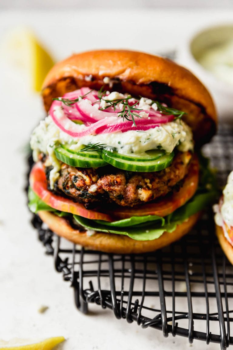 Close up view of a feta spinach turkey burger topped with picked red onions and cucumber slices. 
