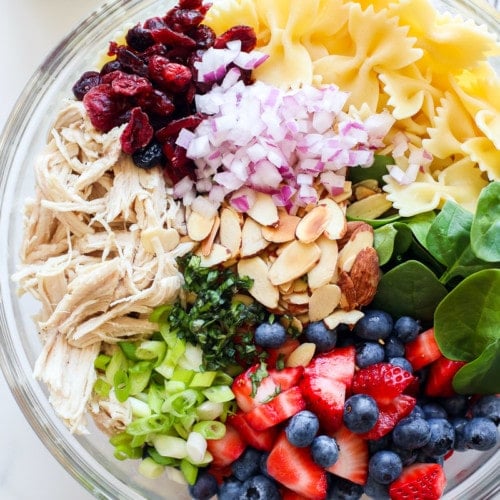Ingredient for Summer Pasta Salad with Chicken and Berries in a large, glass mixing bowl.
