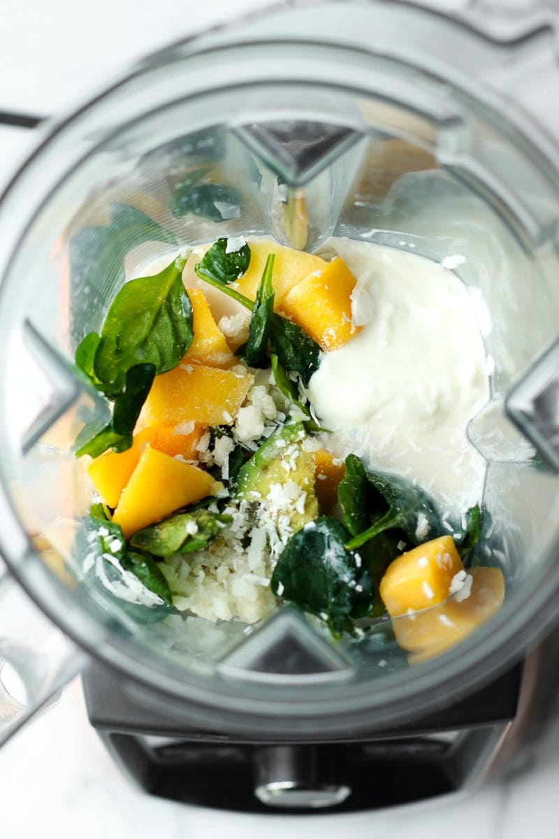 All ingredients for mango avocado energy smoothie in a blender cup