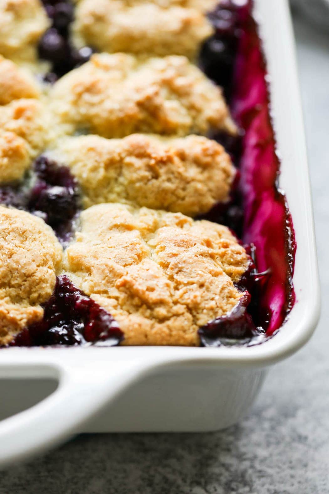 Close up side view blueberry cobbler with biscuit topping in white baking dish
