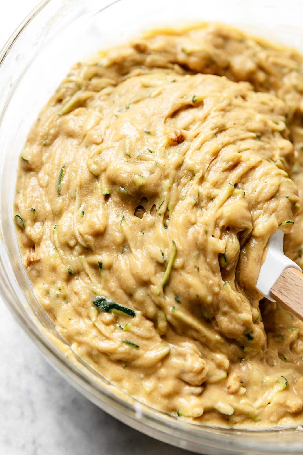 Zucchini bread batter being stirred together in a glass mixing bowl with a spatula