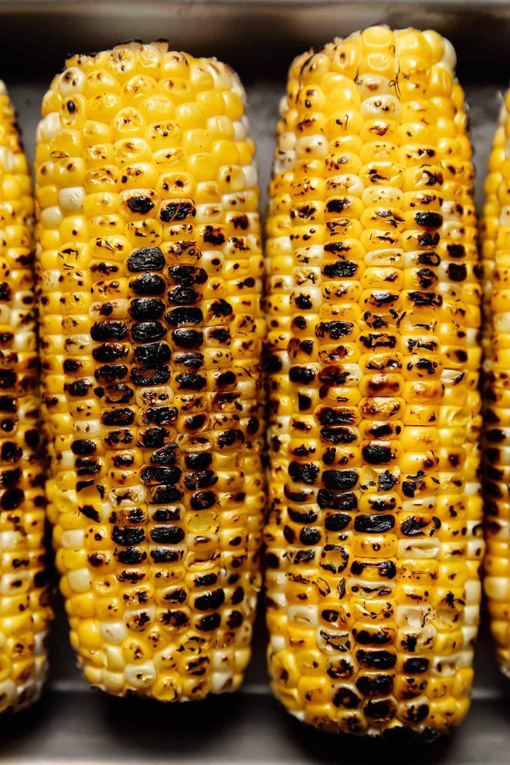 Close up view of grilled corn on the cob showing the browning from the grill on the yellow kernels.