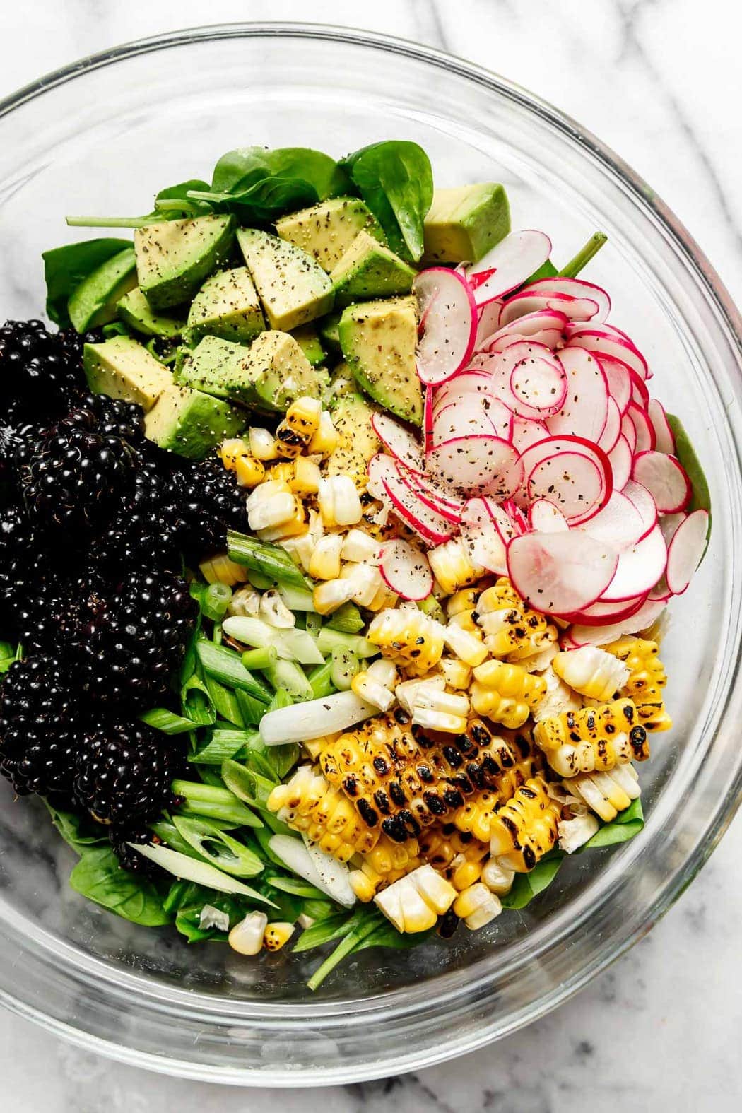 Glass bowl filled with ingredients for Grilled Corn Salad With Blackberries. 