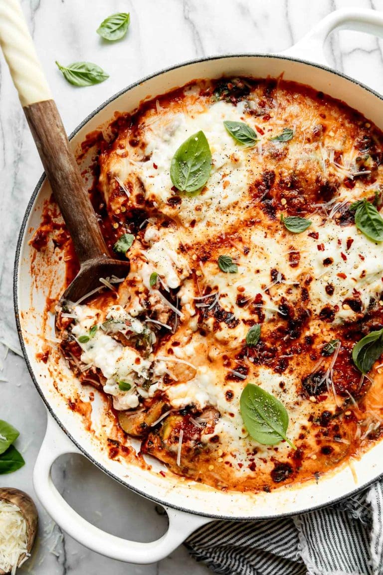 White skillet with zucchini lasagna topped with melted cheese and fresh basil.