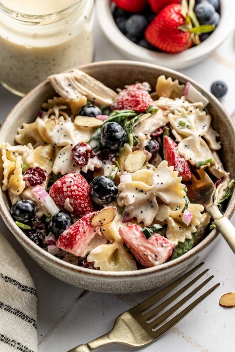 Close up view of a bowl of berry pasta salad with chicken pieces topped with sliced almonds and poppy seed dressing.