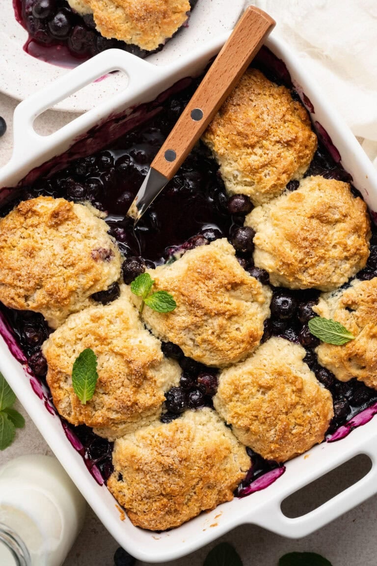 Overhead view of a square baking dish filled with Blueberry Cobbler and topped with mint leaves.