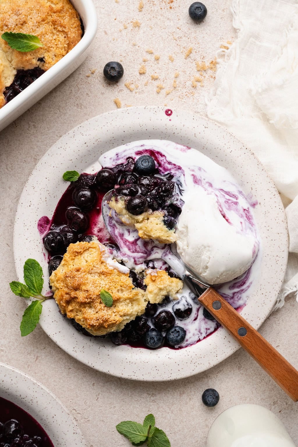 Overhead view of a plate filled with a serving of Blueberry Cobbler with a scoop of ice cream on the side.