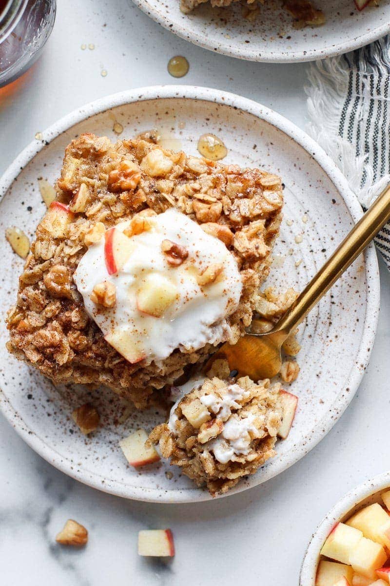 Overhead view apple cinnamon baked oatmeal on stone plate topped with yogurt, diced apples and maple syrup.