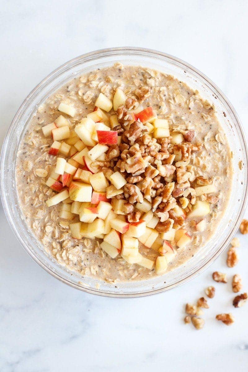 Overhead view of a glass bowl filled with Baked Apple Cinnamon Oatmeal ingredients with apple pieces and walnuts on top