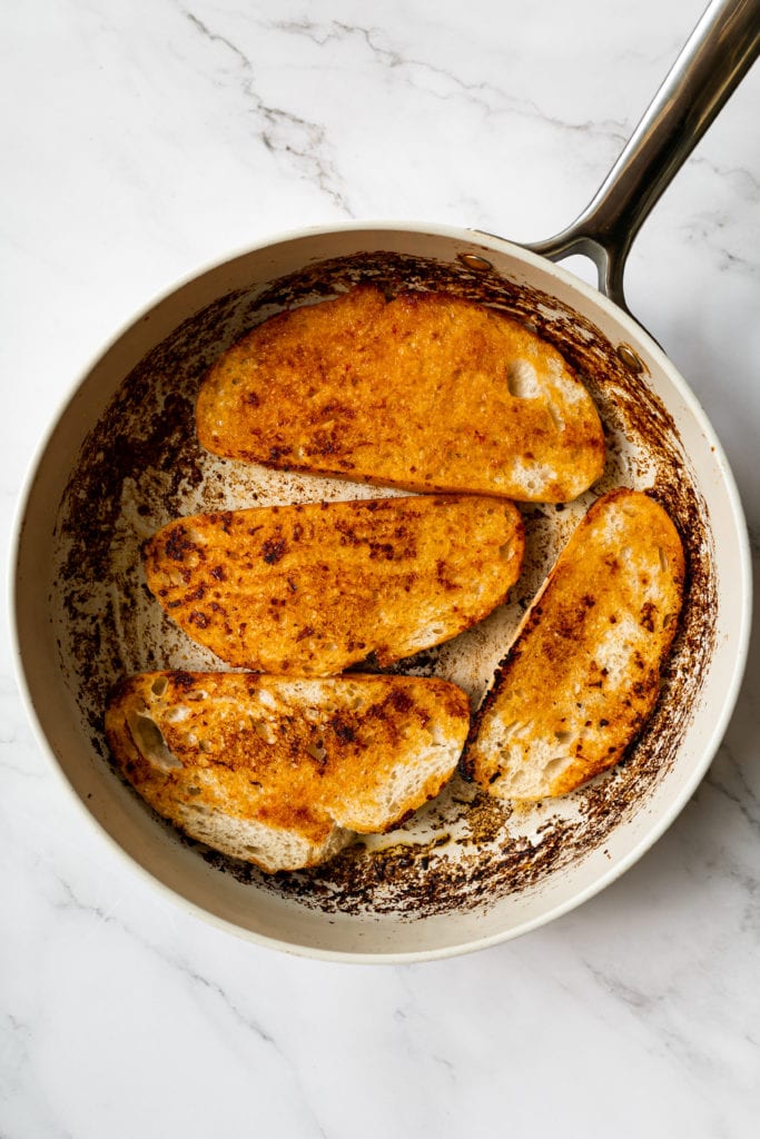 Four slices of crusty bread being toasted in a skillet