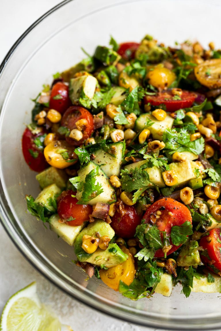 Summer corn salad in clear glass mixing bowl with diced avocado and fresh cilantro