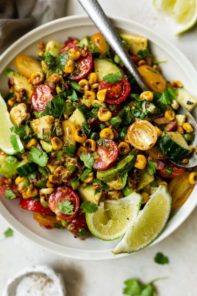 A vibrant colored corn and avocado salad tossed in chili-lime vinaigrette served in a white bowl