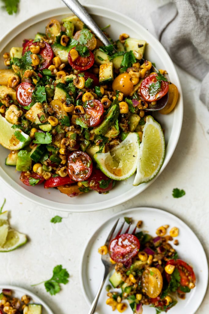 Overhead view of a corn and avocado salad served in a white bowl topped with cilantro and lime wedges