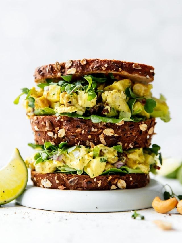 Two overfilled curry chicken salad sandwiches stacked on top of each other on a white plate