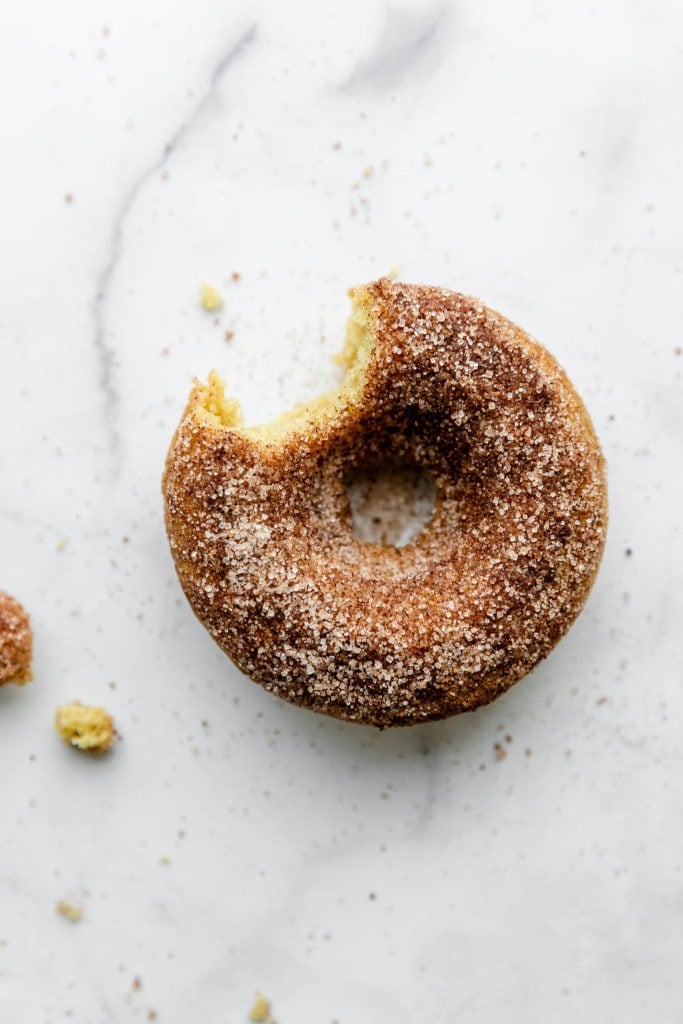 A cinnamon sugar gluten-free baked donut with a bite taken from it laying on a marbled counter.