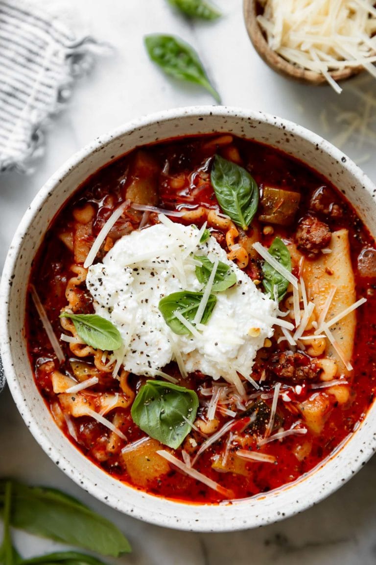 White bowl filled with Lasagna Soup topped with cheese and fresh basil. 
