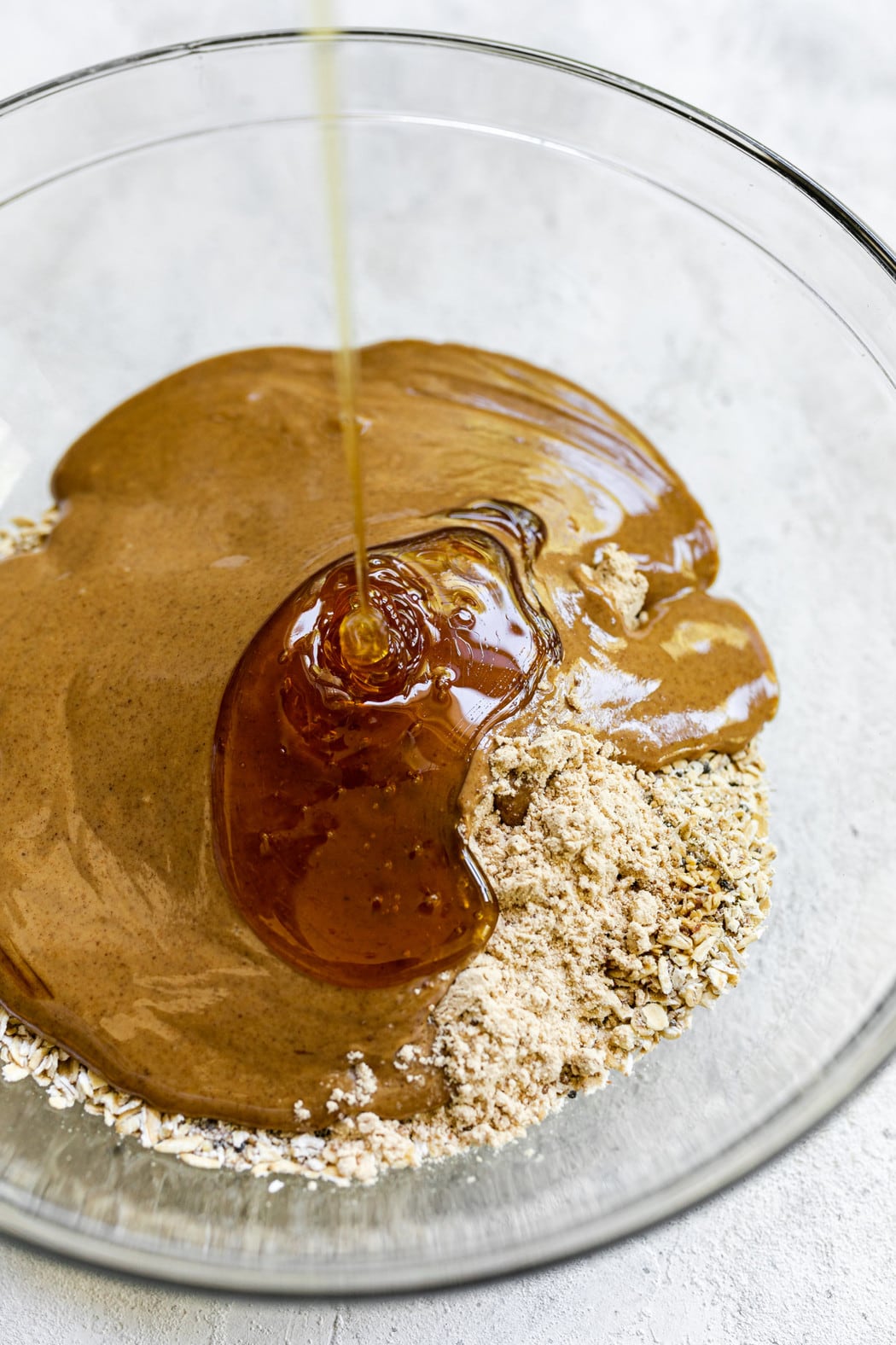 Honey being poured into mixing bowl filled with other ingredients for monster cookie energy bites. 