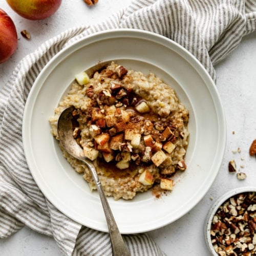 Instant Pot Apple Cinnamon Oatmeal in a white bowl topped with apple chunks, pecans, and maple syrup.