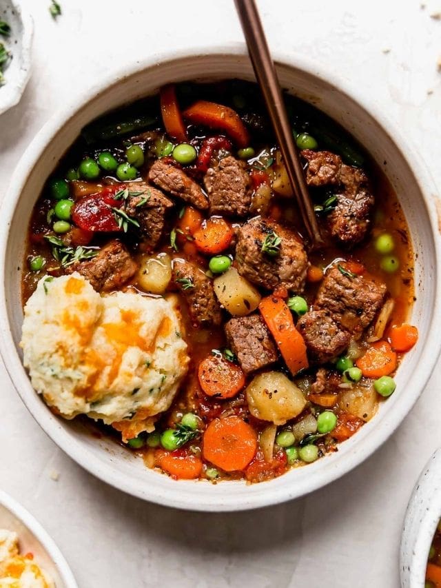 Overhead view of vegetable beef soup with a cheddar biscuit in the bowl.